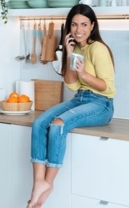 Femme qui boit un café assise sur le plan de travail d'une cuisine moderne